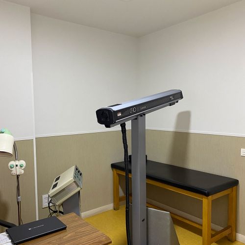 Imagen de sala con aparato para sesión de fisioterapia y banco al fondo