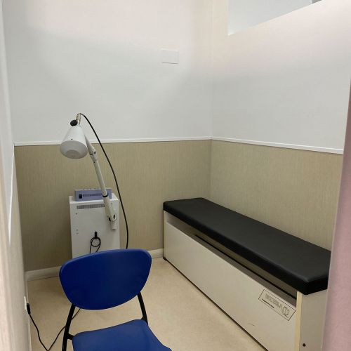 Sala con silla azul en primer plano, banco a la derecha y aparato de electroterapia detrás
